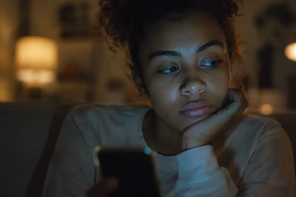 Close-up of a person's face lit by a phone screen, glancing away