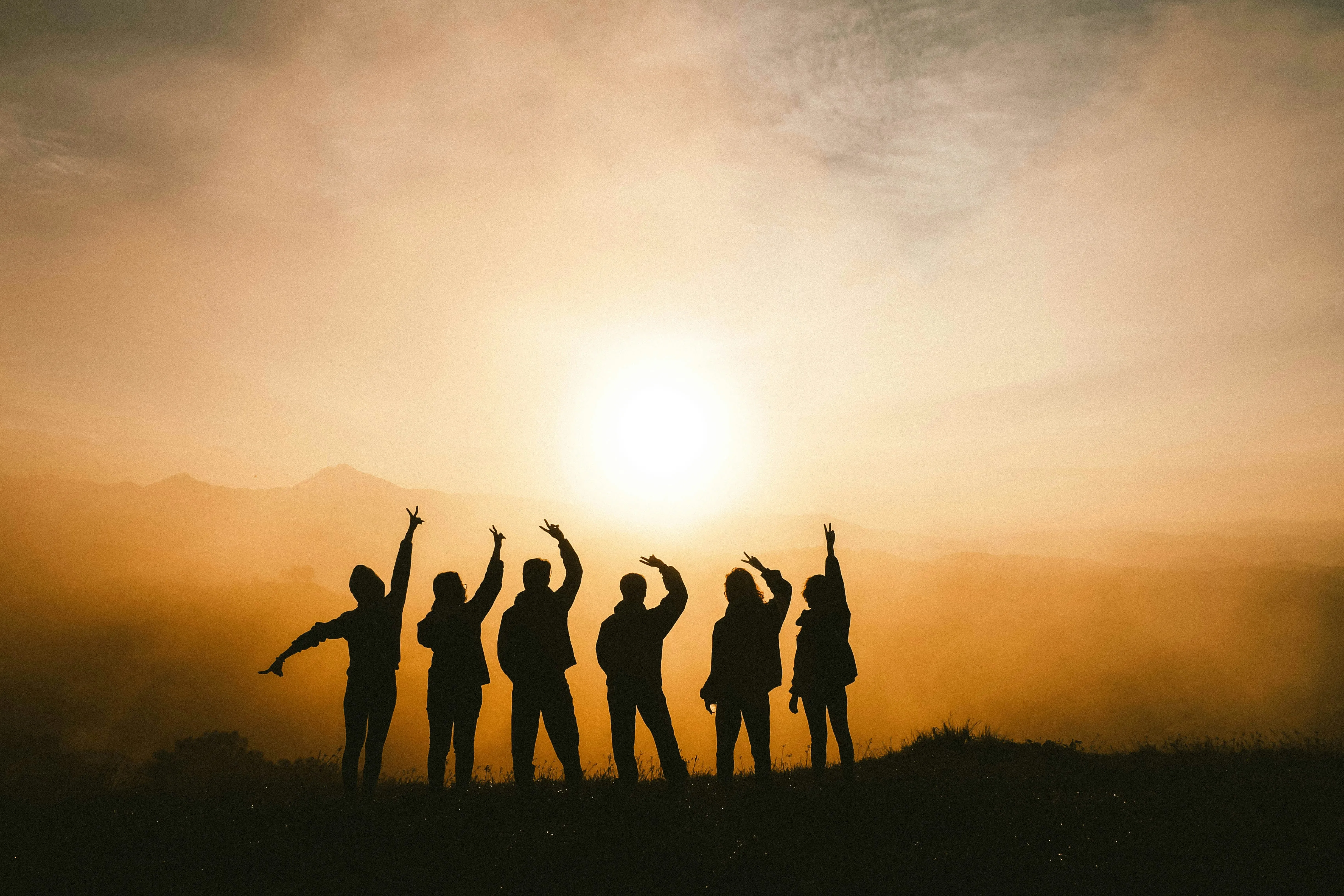 A group of people on a hill facing a red sunset