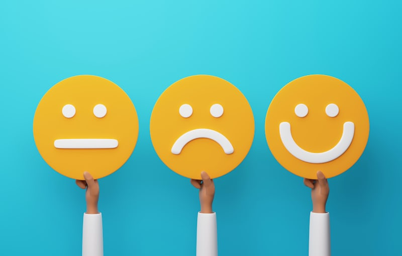 hands holding up a neutral, sad and smiley face emojis made of yellow cardboard side by side